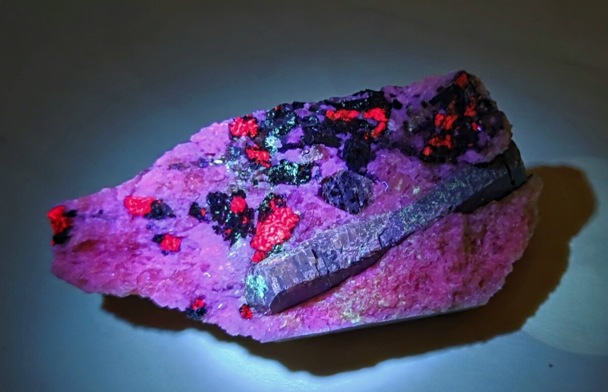 UV Pink rock slab with bright red crystalline patches and dark purple inclusions illuminated from below.